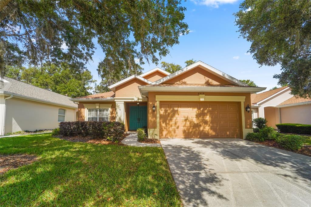 A single-story house with a tan stucco exterior, a two-car garage, and a teal front door — 4413 CALIQUEN DRIVE, BROOKSVILLE, FL