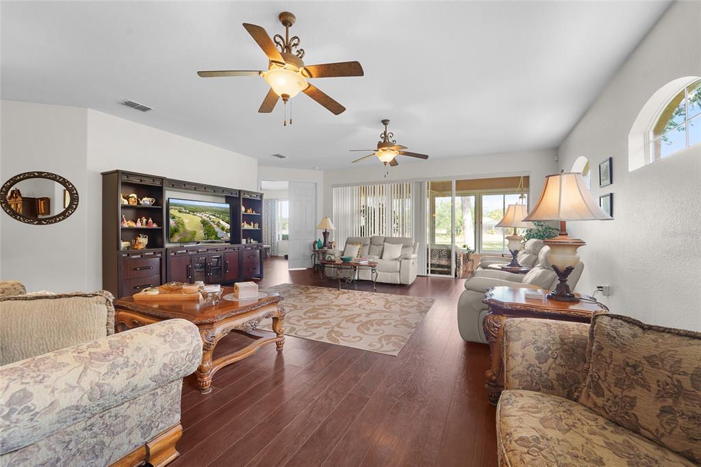 A living room features dark wood flooring, two ceiling fans, and an entertainment center — 4413 CALIQUEN DRIVE, BROOKSVILLE, FL