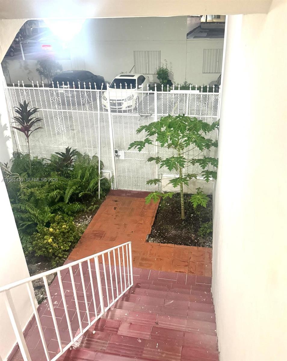 A view looking down outdoor stairs toward a gated courtyard with plants and parked cars — 755 SW 6th St # 6, Miami FL 33130, MIAMI, FL
