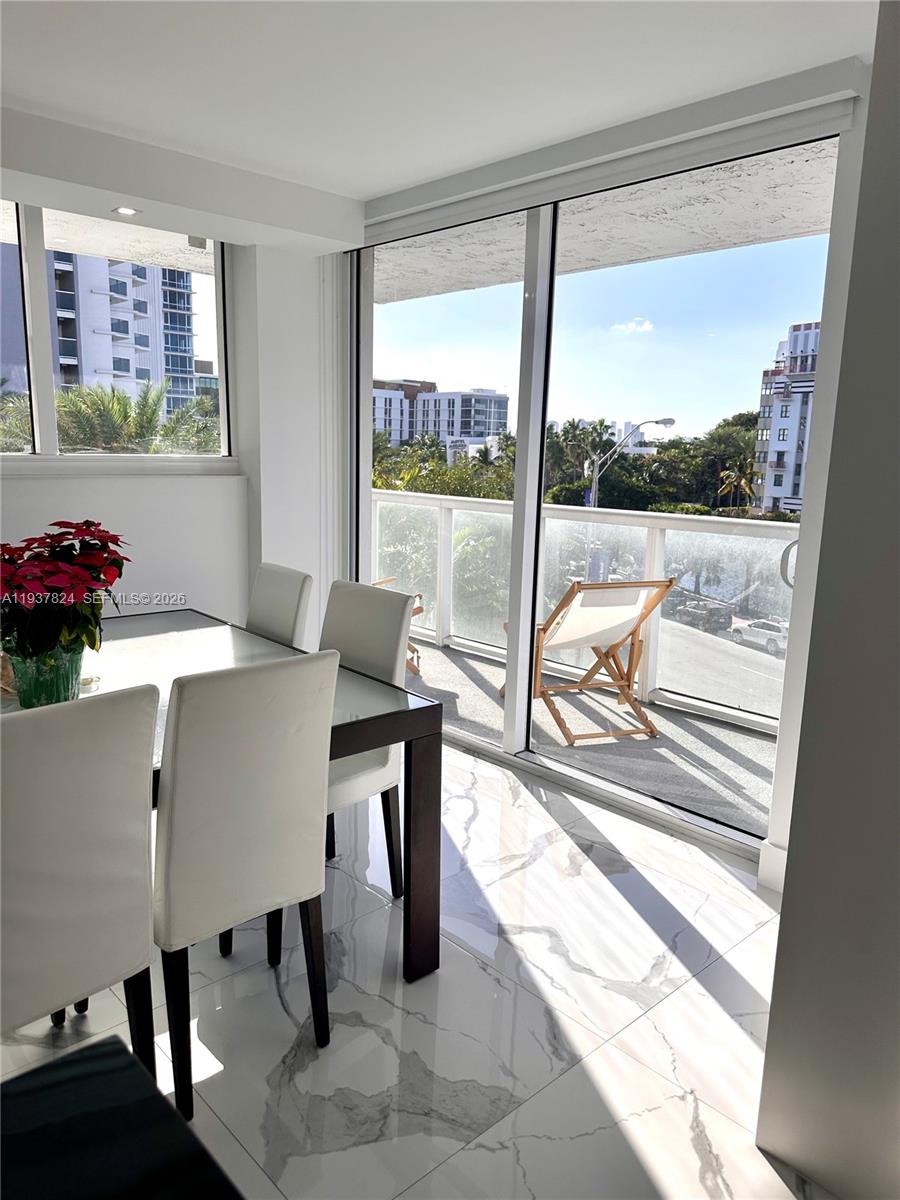 A dining area with a glass table, white chairs, marble floors, and a balcony view — 2457 Collins Ave # 408, Miami Beach FL 33140, MIAMI BEACH, FL