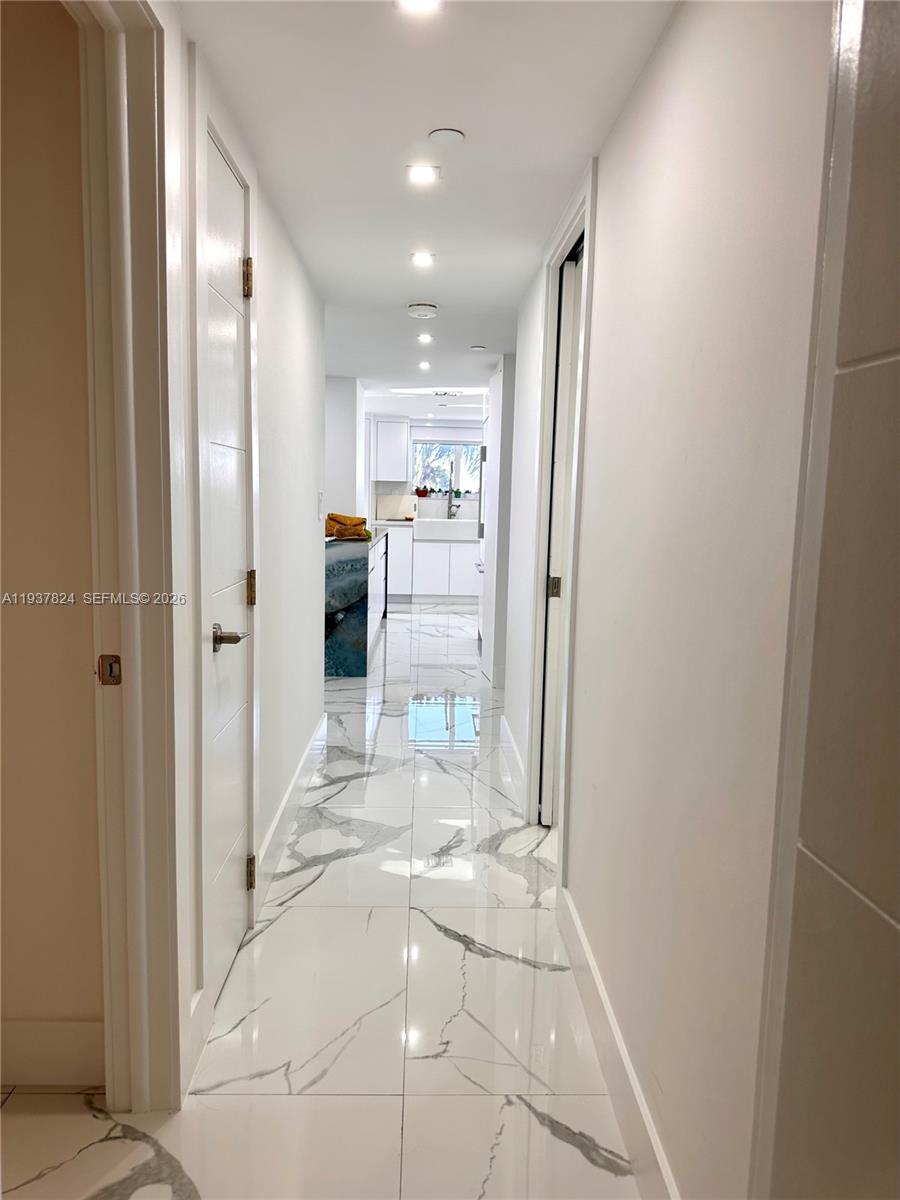 A narrow hallway with white marble-patterned tile floors leads to a bright kitchen — 2457 Collins Ave # 408, Miami Beach FL 33140, MIAMI BEACH, FL