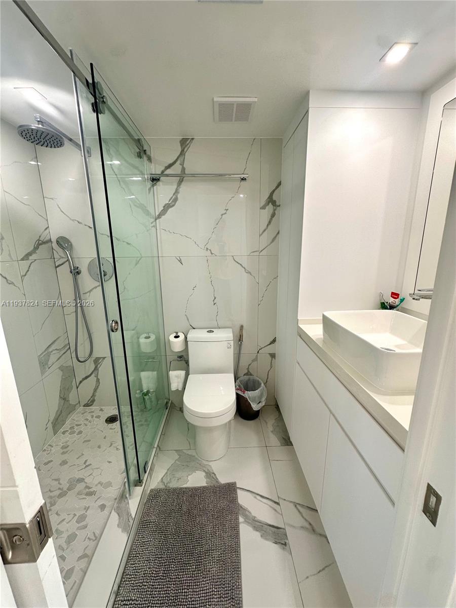 A modern bathroom features a glass-enclosed shower, white marble-style tile, and a vessel sink — 2457 Collins Ave # 408, Miami Beach FL 33140, MIAMI BEACH, FL