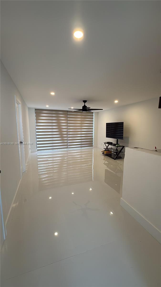 A minimalist living room features white walls, glossy tile flooring, a ceiling fan, and blinds — 1357 NE Ocean Blvd # 311, Stuart FL 34996, STUART, FL