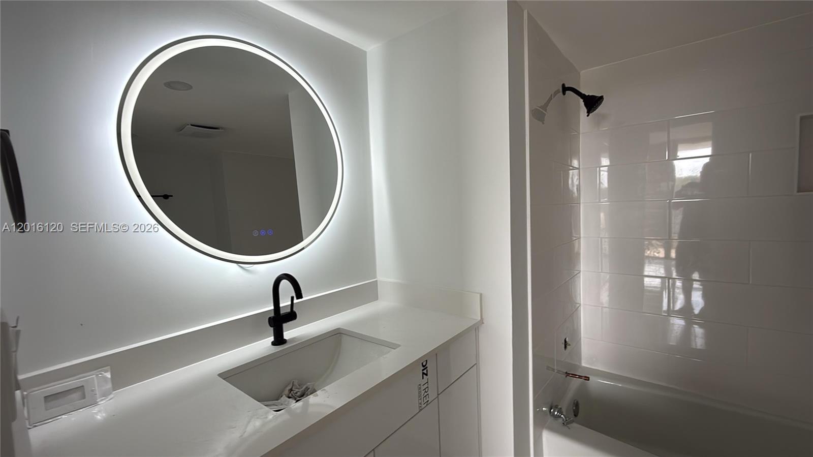 A modern bathroom features a white vanity, a round LED mirror, and a tiled shower — 1357 NE Ocean Blvd # 311, Stuart FL 34996, STUART, FL