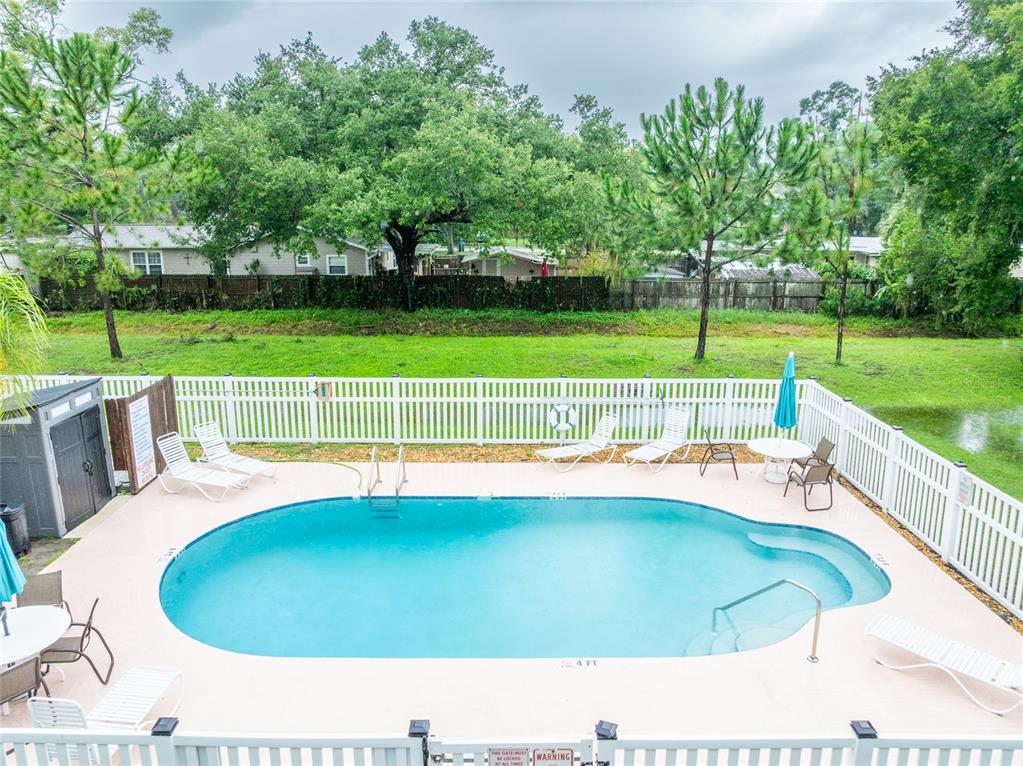 An elevated view of a backyard swimming pool surrounded by a white fence and trees — 1944 ELAINE DRIVE UNIT 1944, CLEARWATER, FL