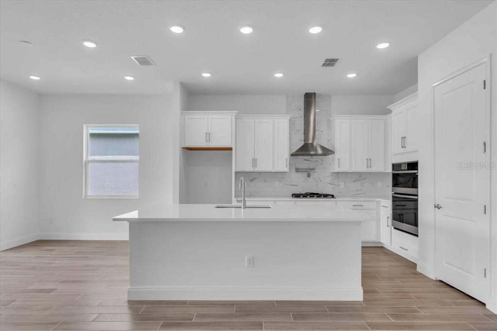 A modern kitchen features white cabinetry, a large central island, and stainless steel appliances — 2302 LONE TREE BEND, ZEPHYRHILLS, FL