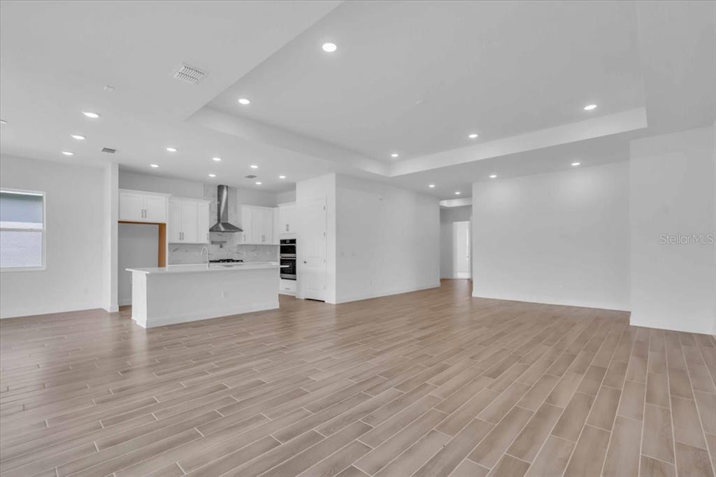 A modern open-concept kitchen and living area features white cabinetry, recessed lighting, and wood-look flooring — 2302 LONE TREE BEND, ZEPHYRHILLS, FL