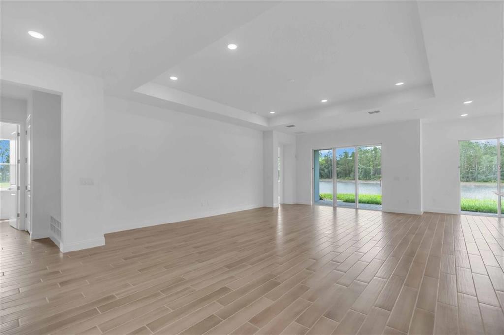 An empty living room with light wood-look tile floors, recessed lighting, and sliding glass doors — 2302 LONE TREE BEND, ZEPHYRHILLS, FL