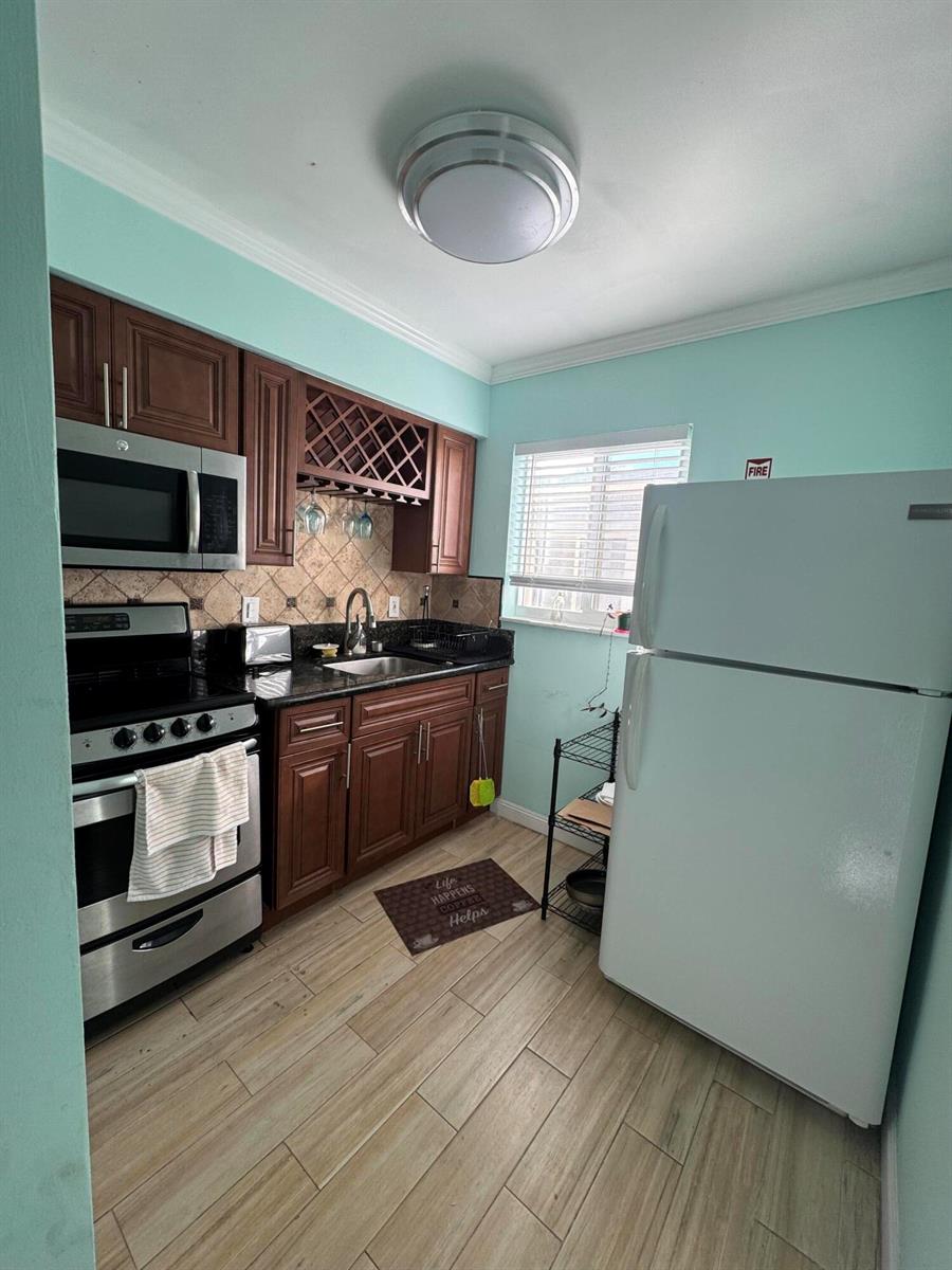 A kitchen features wood cabinets, dark countertops, stainless steel appliances, and light-colored tile flooring — 323 Monroe Street # 6, Hollywood FL 33019, HOLLYWOOD, FL