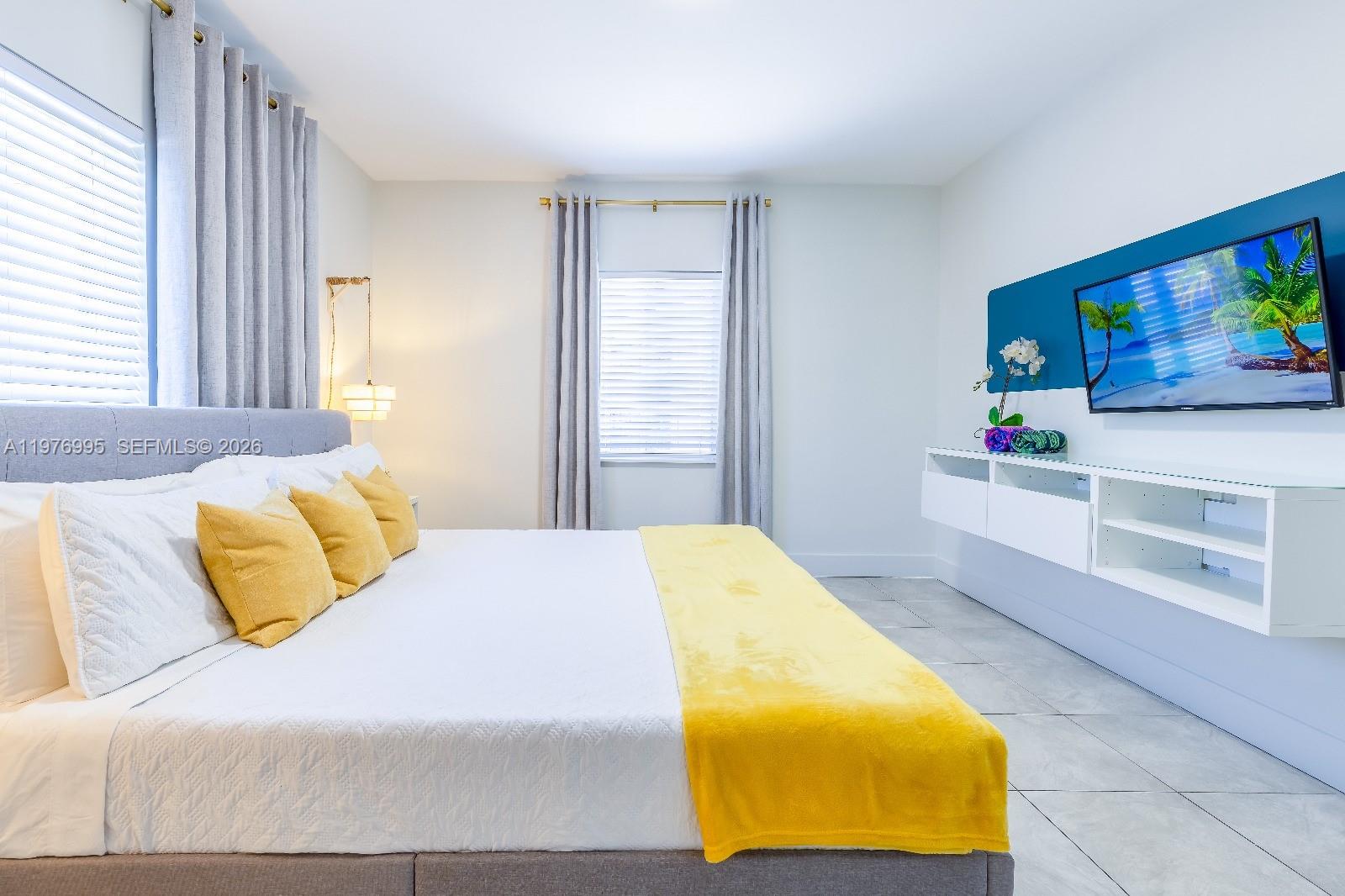 A bedroom features a bed with yellow accents, gray curtains, and a wall-mounted television — 1836 NW 16th Ter, Miami FL 33125, MIAMI, FL