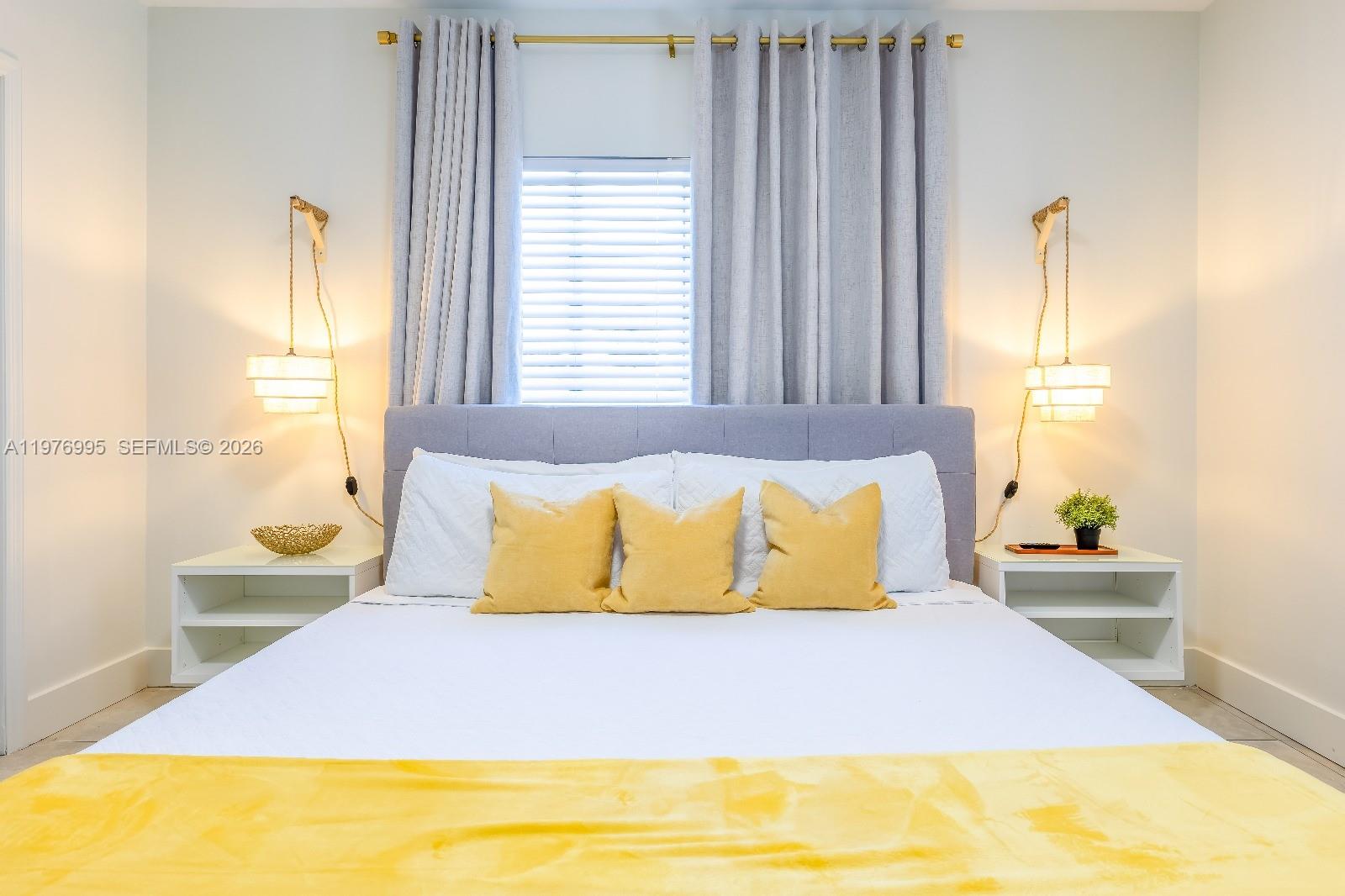 A bedroom features a bed with yellow accents, gray curtains, and wall-mounted pendant lights — 1836 NW 16th Ter, Miami FL 33125, MIAMI, FL