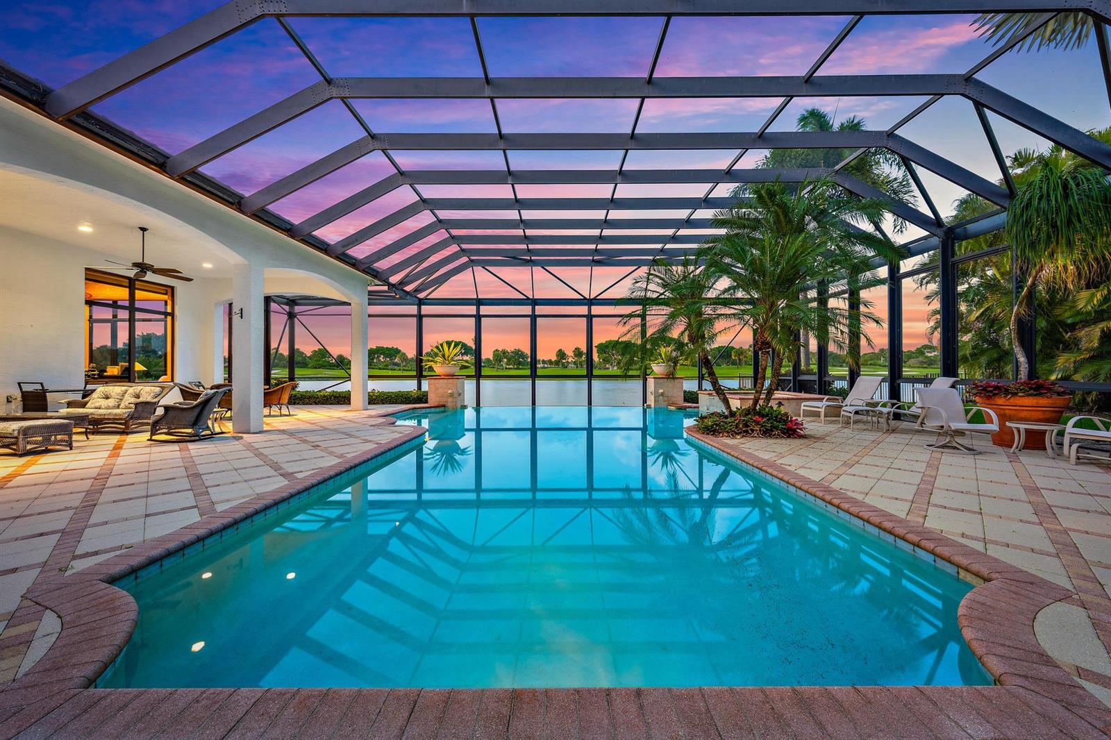 A screened-in pool patio overlooks a lake at sunset with palm trees and lounge chairs — 7170 Winding Bay Lane, West Palm Beach FL 33412, WEST PALM BEACH, FL
