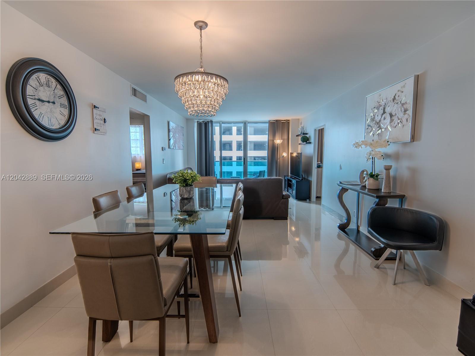 A dining area with a glass table, crystal chandelier, and tile flooring opens to a living room — 4001 S Ocean Dr # 8J, Hollywood FL 33019, HOLLYWOOD, FL