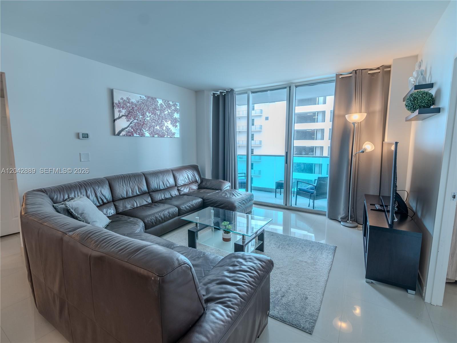 A living room features a large brown leather sectional, glass coffee table, and balcony access — 4001 S Ocean Dr # 8J, Hollywood FL 33019, HOLLYWOOD, FL