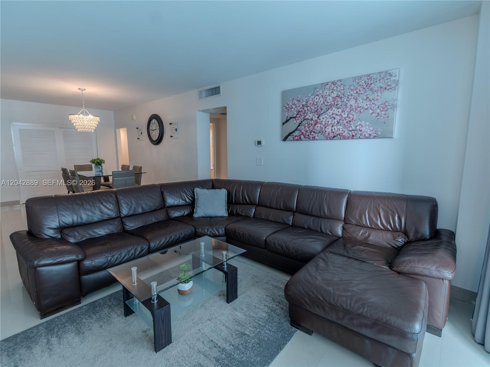 A living room features a large brown leather sectional, a glass coffee table, and wall art — 4001 S Ocean Dr # 8J, Hollywood FL 33019, HOLLYWOOD, FL