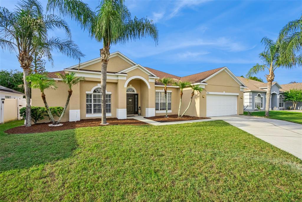 A single-story tan stucco house with a two-car garage and palm trees in the yard — 13805 EAGLES GLEN COURT, ORLANDO, FL
