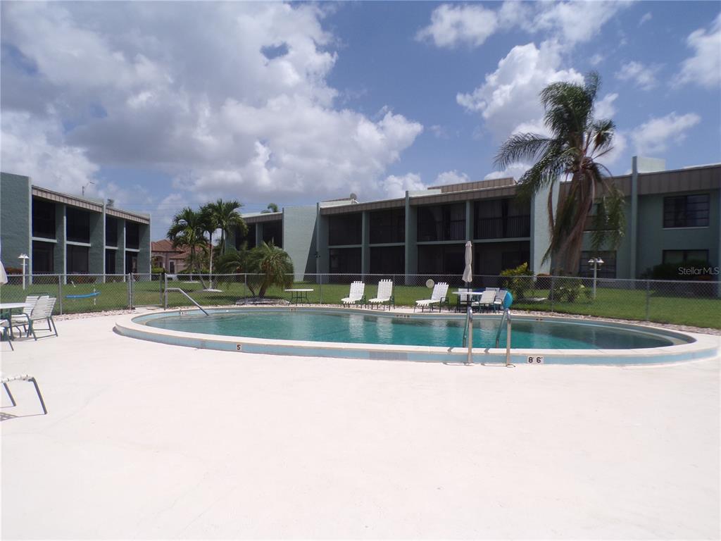 An oval swimming pool sits in front of two-story apartment buildings with screened balconies — 1461 AQUI ESTA DRIVE UNIT B4, PUNTA GORDA, FL