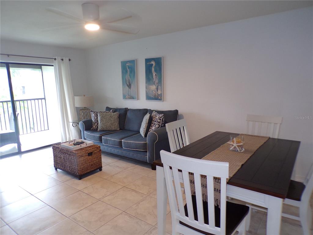 A living and dining area features a blue sofa, white chairs, and tile flooring — 1461 AQUI ESTA DRIVE UNIT B4, PUNTA GORDA, FL
