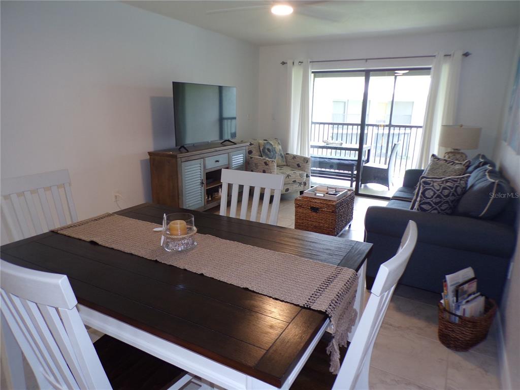 A dining area with a dark wood table opens into a living room with balcony access — 1461 AQUI ESTA DRIVE UNIT B4, PUNTA GORDA, FL