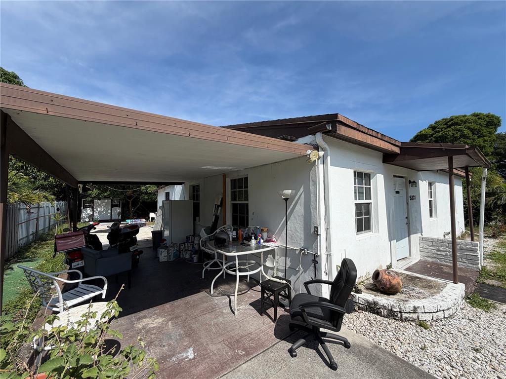 A white house exterior features a covered carport with outdoor furniture and a front entrance — 15331 NW 27TH PLACE, OPA LOCKA, FL