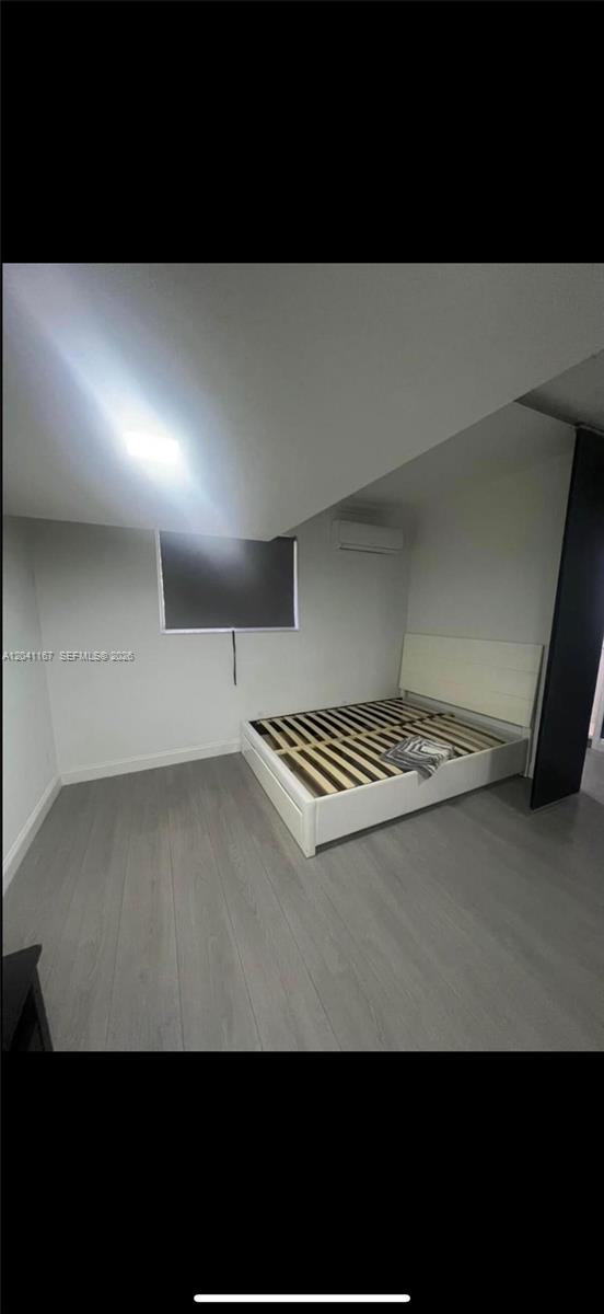 A bedroom with gray wood-look flooring, a white bed frame, and a wall-mounted air conditioner — 4731 fillmore # 1, Hollywood FL 33021, HOLLYWOOD, FL