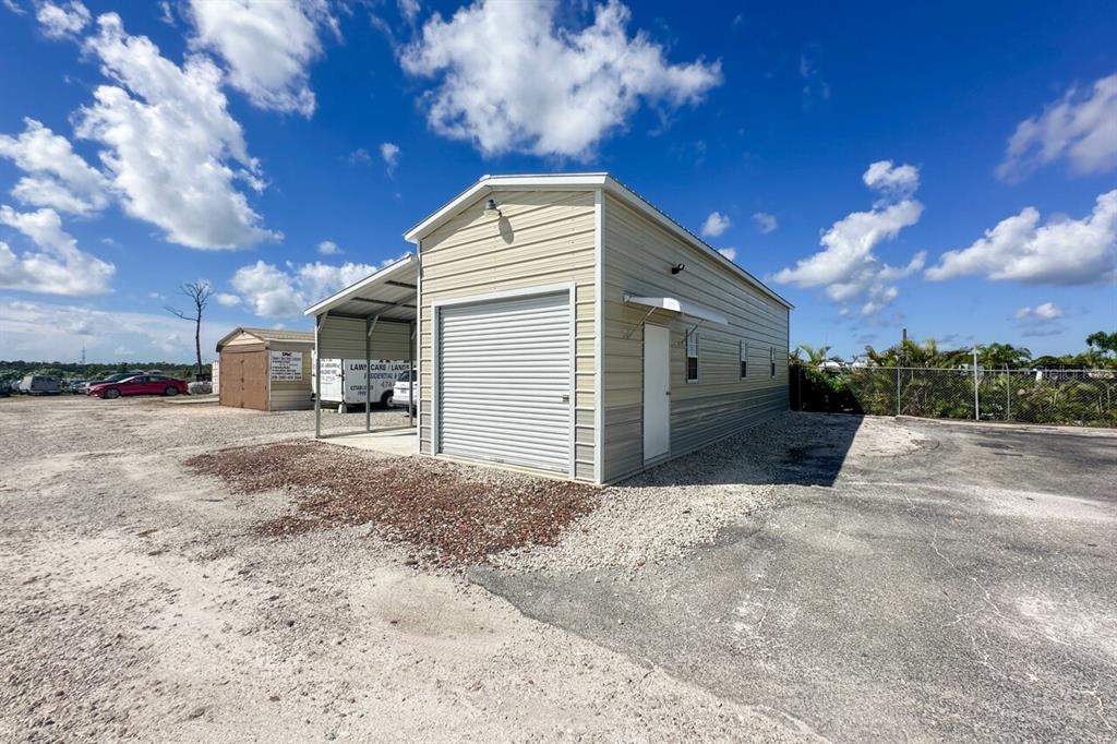 A metal storage building with a roll-up garage door, side entrance, and attached carport — 2820 AVENUE OF THE AMERICAS, ENGLEWOOD, FL