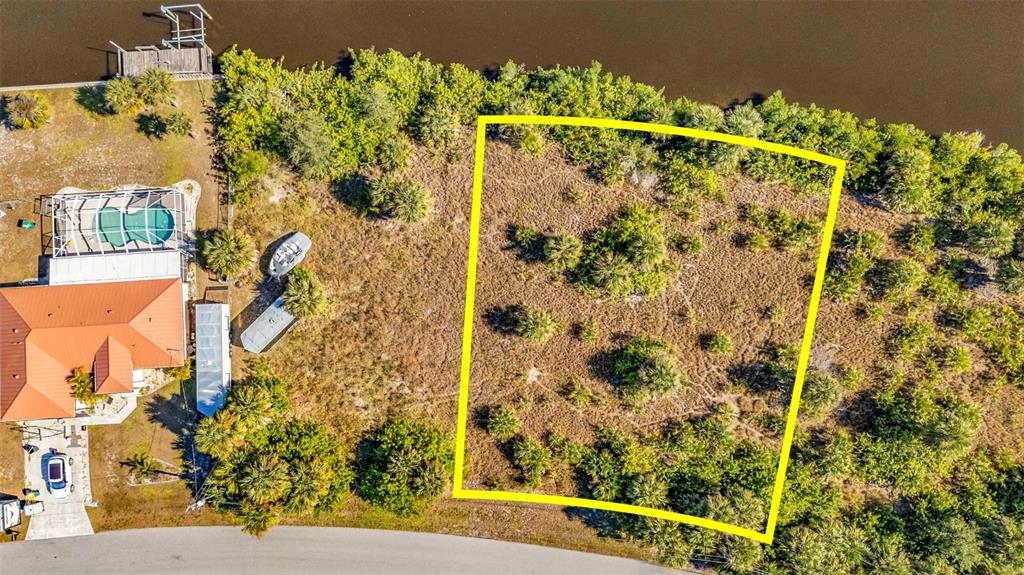 An aerial view shows a vacant, rectangular waterfront lot outlined in yellow next to a house — 4298 LIBRARY STREET, PORT CHARLOTTE, FL
