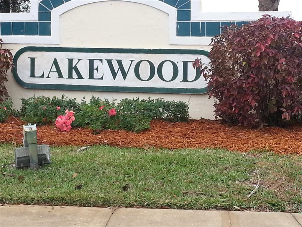 A sign reading Lakewood stands in a landscaped garden bed with mulch and shrubs — 13829 TIMBERLAND DRIVE UNIT 203, ORLANDO, FL