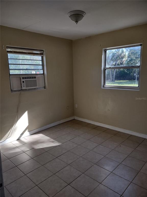 An empty room features beige walls, tiled flooring, two windows, and a ceiling light fixture — 157 E NORTHSIDE DRIVE UNIT 1, LAKE WALES, FL