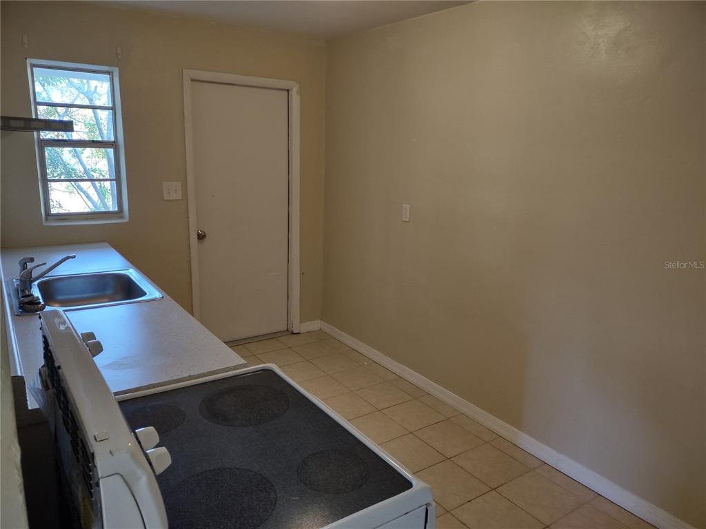A kitchen features a white electric stove, a stainless steel sink, and beige tile flooring — 157 E NORTHSIDE DRIVE UNIT 1, LAKE WALES, FL