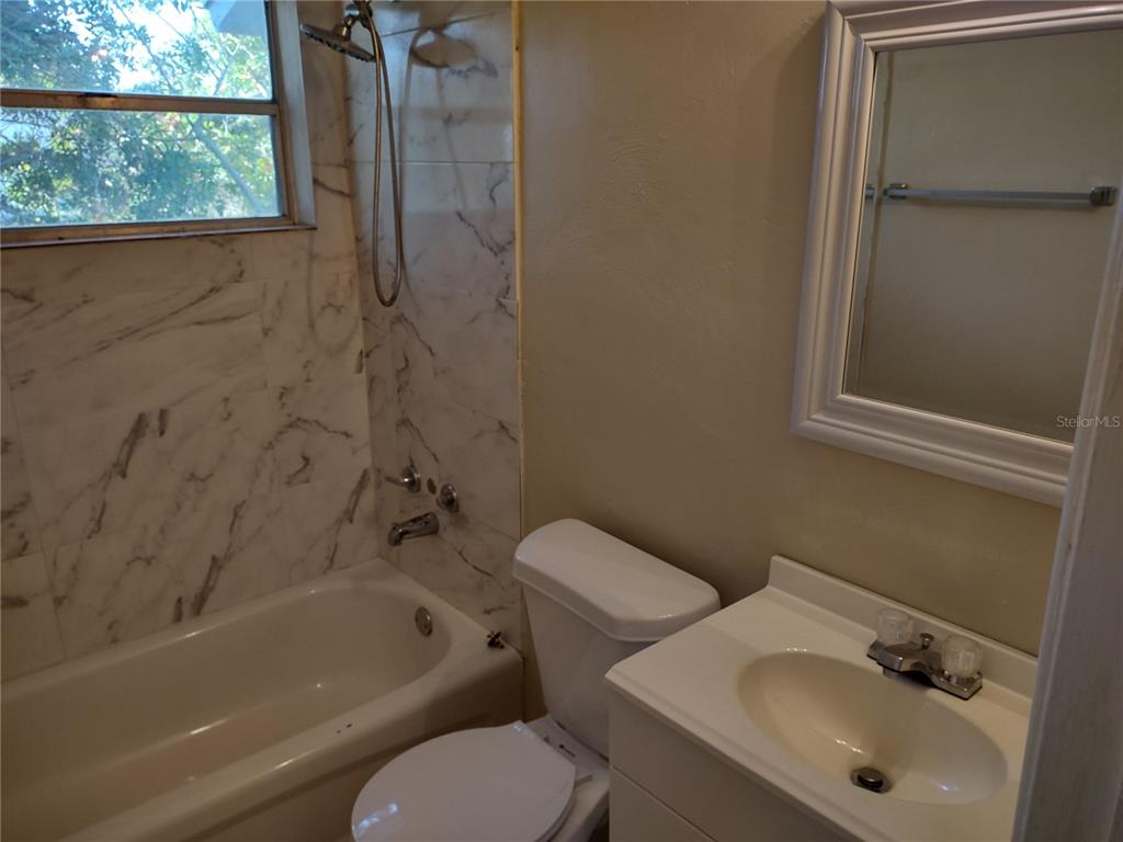 A bathroom features a white vanity, a toilet, and a bathtub with marble-patterned tile walls — 157 E NORTHSIDE DRIVE UNIT 1, LAKE WALES, FL