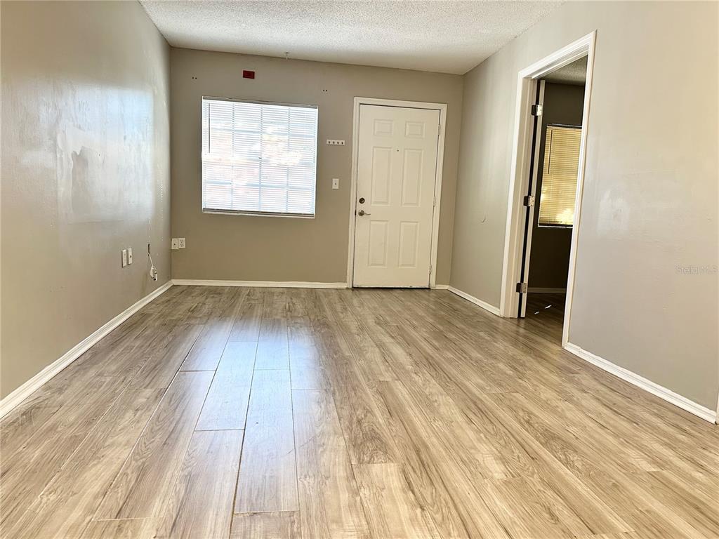 An empty room features light-colored wood-look flooring, gray walls, a window, and a white door — 2517 CAPER LANE UNIT 205, MAITLAND, FL