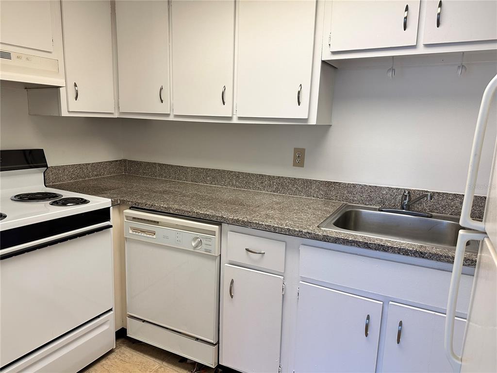 A kitchen features white cabinets, granite-look countertops, a white dishwasher, and a stainless steel sink — 2517 CAPER LANE UNIT 205, MAITLAND, FL
