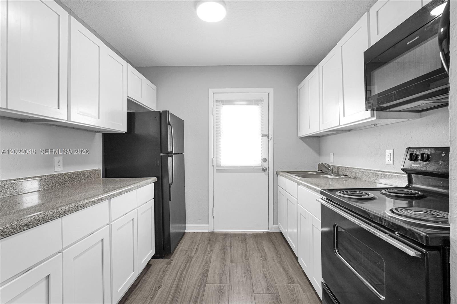 A galley kitchen features white cabinets, black appliances, granite countertops, and wood-look flooring — 400 NW 65th Ave # 210, Margate FL 33063, MARGATE, FL