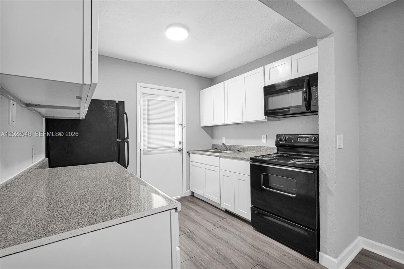 A kitchen features white cabinets, black appliances, granite-look countertops, and wood-look flooring — 400 NW 65th Ave # 210, Margate FL 33063, MARGATE, FL