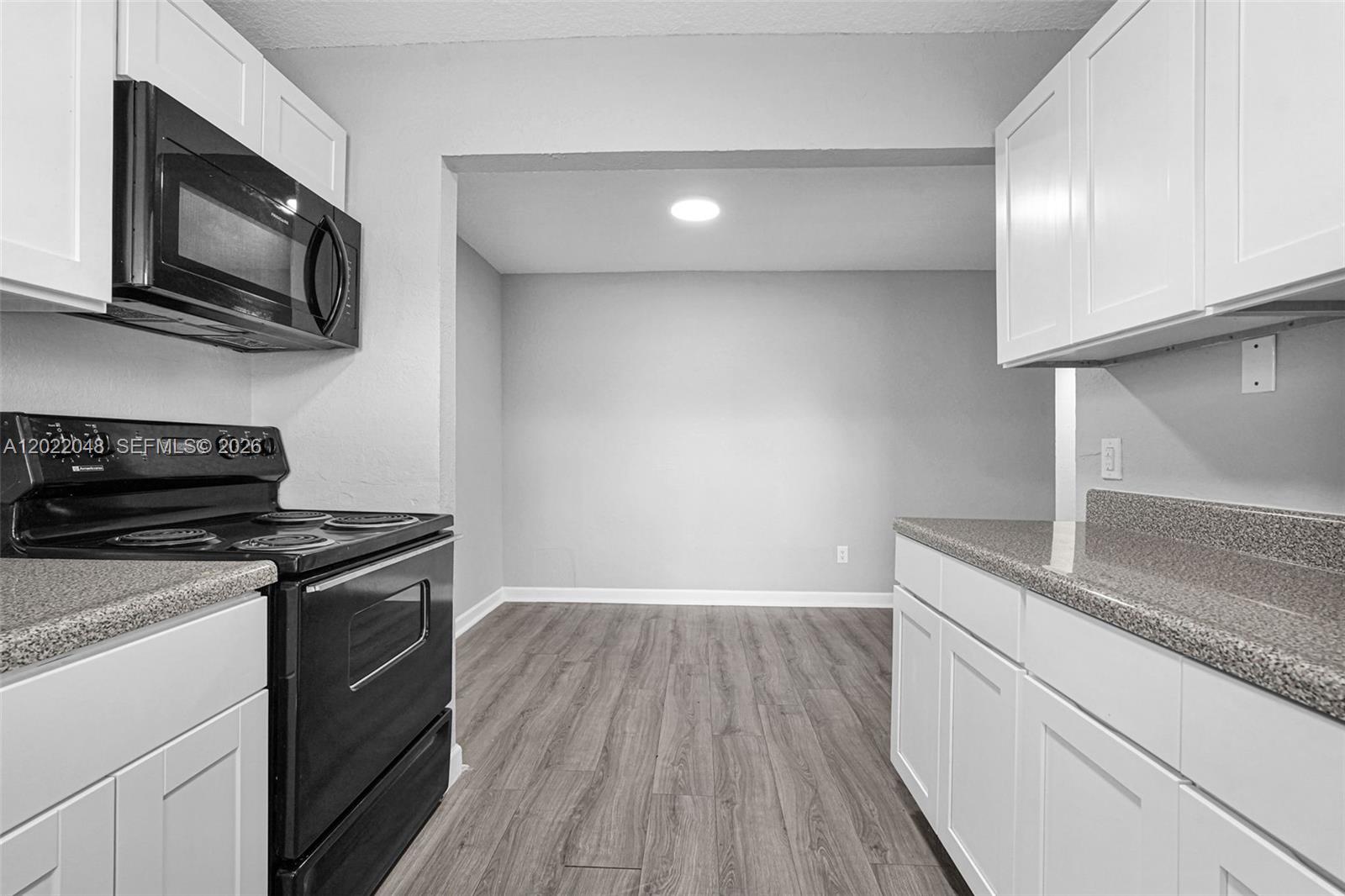 A kitchen features white cabinets, black appliances, speckled countertops, and wood-look flooring — 400 NW 65th Ave # 210, Margate FL 33063, MARGATE, FL