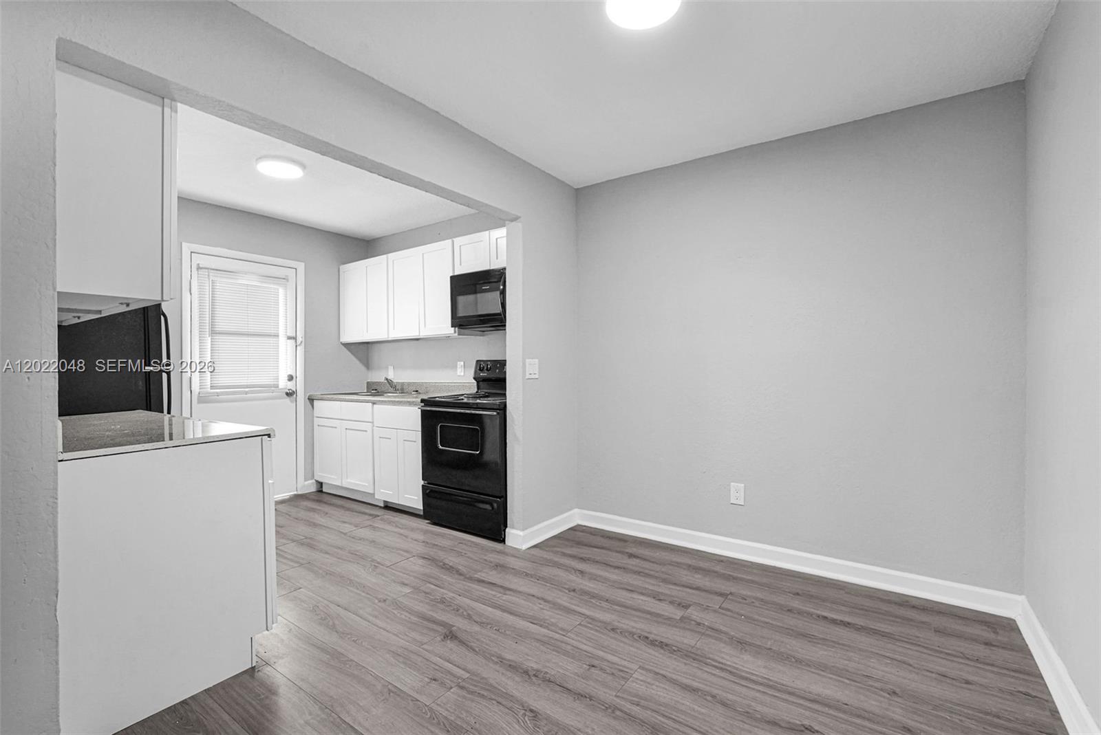 A kitchen with white cabinets, black appliances, and wood-look flooring opens to a dining area — 400 NW 65th Ave # 210, Margate FL 33063, MARGATE, FL
