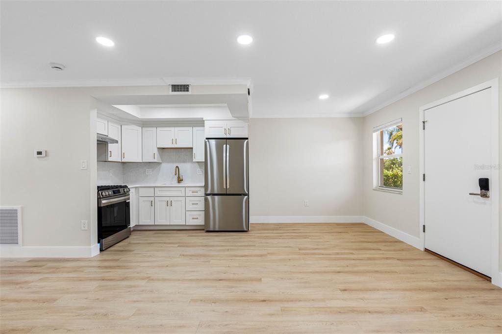 A kitchen with white cabinets and stainless steel appliances opens into a living area — 1 GATESHEAD DRIVE UNIT B108, DUNEDIN, FL