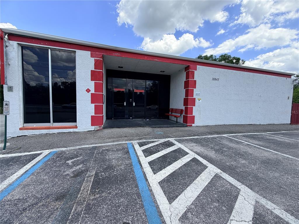 A single-story commercial building features a white stucco exterior with red accents and glass doors — 18843 N 41 HIGHWAY, LUTZ, FL