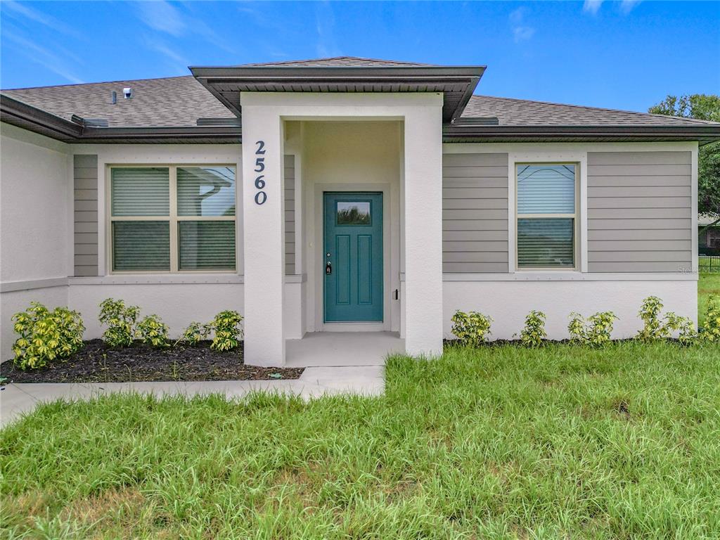 A single-story house exterior features a teal front door, white stucco, and gray siding — 2560 S BISCAYNE DRIVE, NORTH PORT, FL