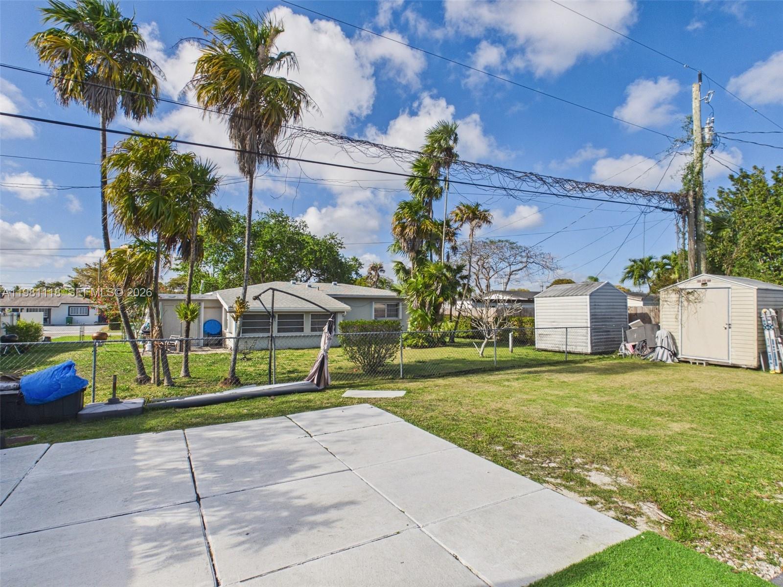 A backyard features a concrete patio, a chain-link fence, palm trees, and two storage sheds — 9911 Haitian Dr, Cutler Bay FL 33189, CUTLER BAY, FL