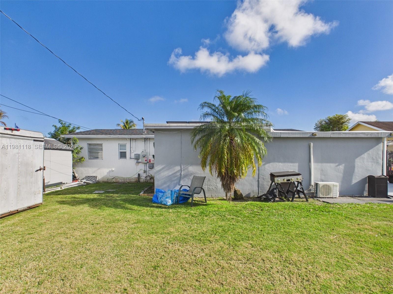 A backyard features a grassy lawn, a palm tree, a grill, and a white house — 9911 Haitian Dr, Cutler Bay FL 33189, CUTLER BAY, FL