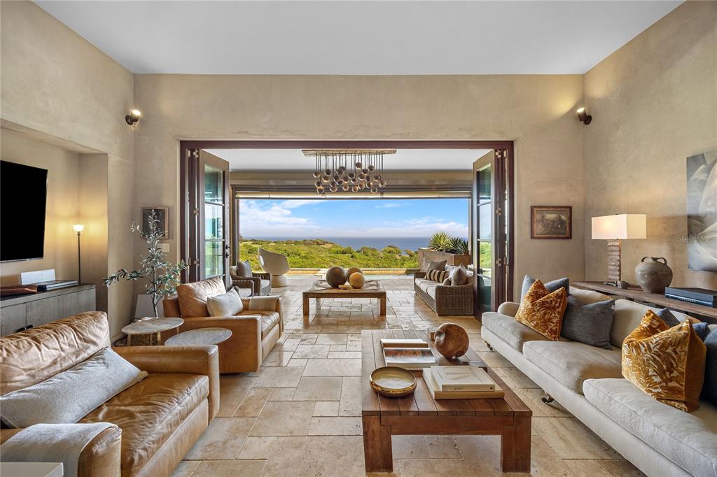 A living room with stone floors and large folding doors opening to an ocean view — 2 OCEAN GOLF VILLA ROYAL ISABELA, ISABELA, PR