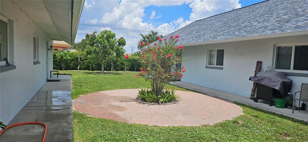 A backyard features a circular brick patio, a flowering tree, and a concrete walkway — 1205 ACADEMY BOULEVARD UNIT B, CAPE CORAL, FL