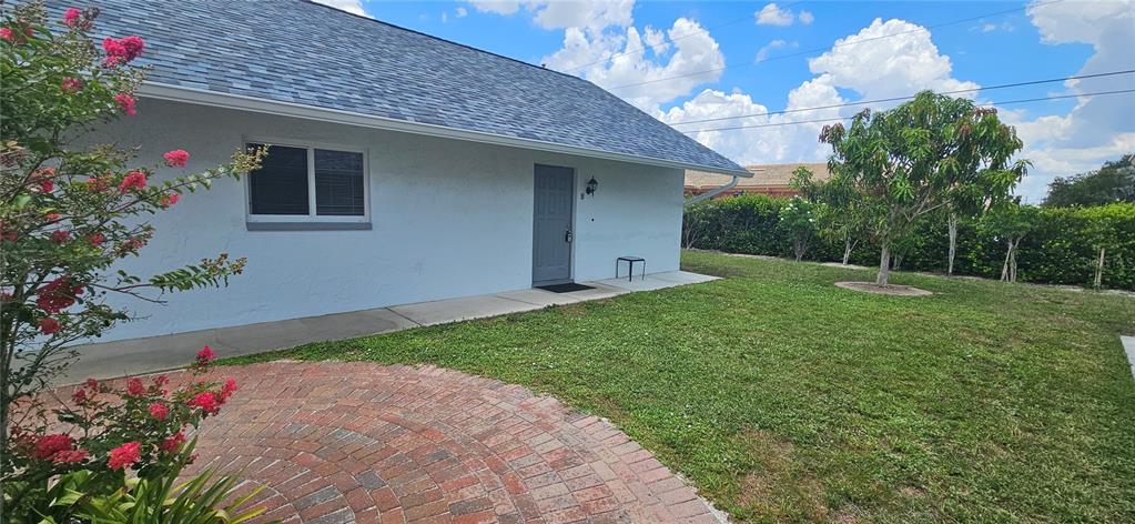 A light blue house exterior features a brick patio, a gray door, and a lawn — 1205 ACADEMY BOULEVARD UNIT B, CAPE CORAL, FL
