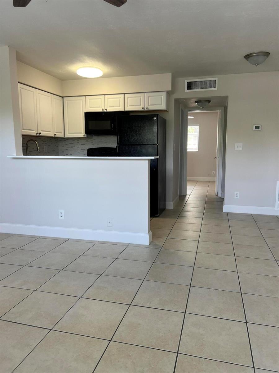 A kitchen with white cabinets and black appliances overlooks a tiled living area — 4670 NE 5th Avenue # 5, Boca Raton FL 33431, BOCA RATON, FL