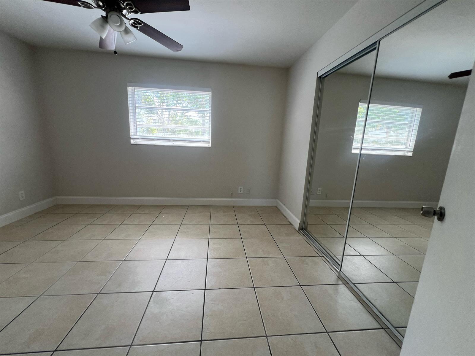 An empty bedroom features beige tile flooring, a ceiling fan, and mirrored sliding closet doors — 4670 NE 5th Avenue # 5, Boca Raton FL 33431, BOCA RATON, FL