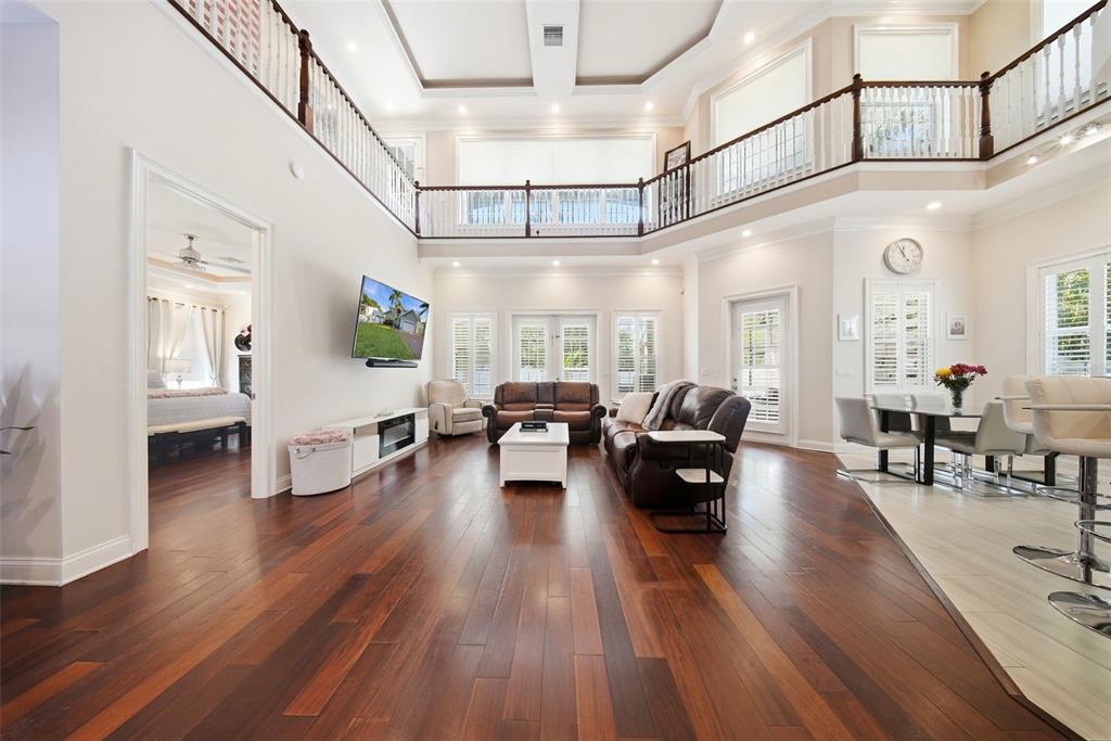 A spacious living room with dark hardwood floors, a two-story ceiling, and a balcony overlook — 234 36TH AVENUE NE, ST PETERSBURG, FL