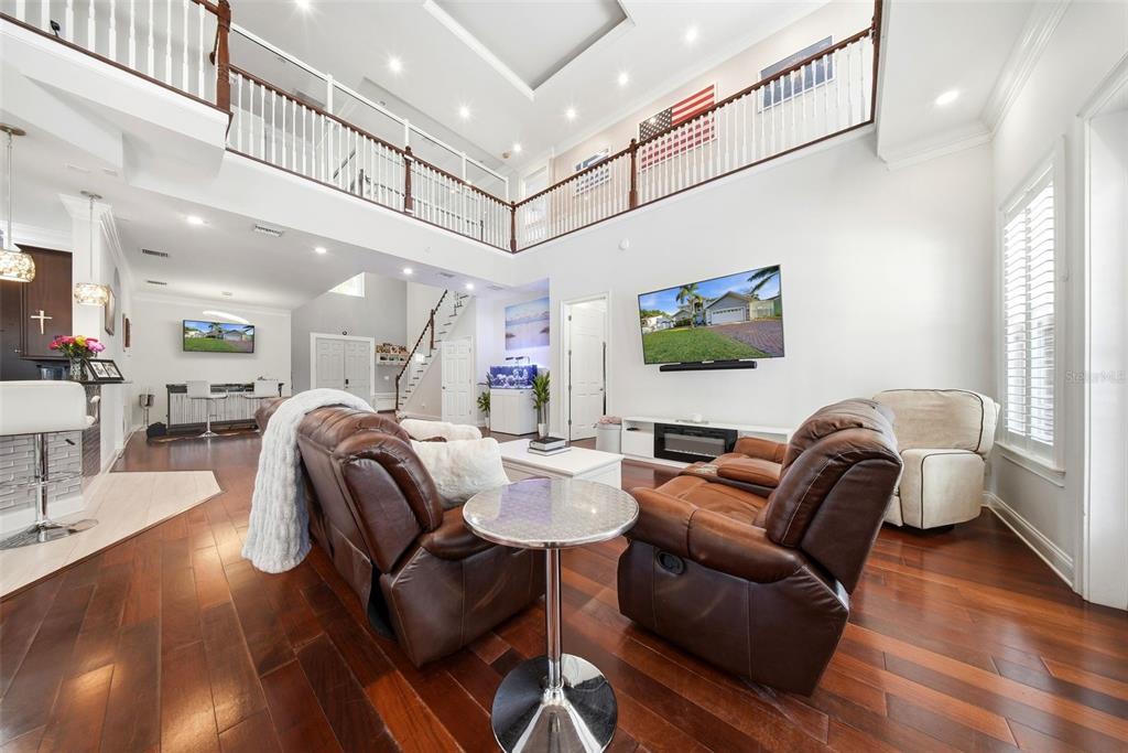 A spacious living room features dark wood floors, a two-story ceiling, and leather seating — 234 36TH AVENUE NE, ST PETERSBURG, FL