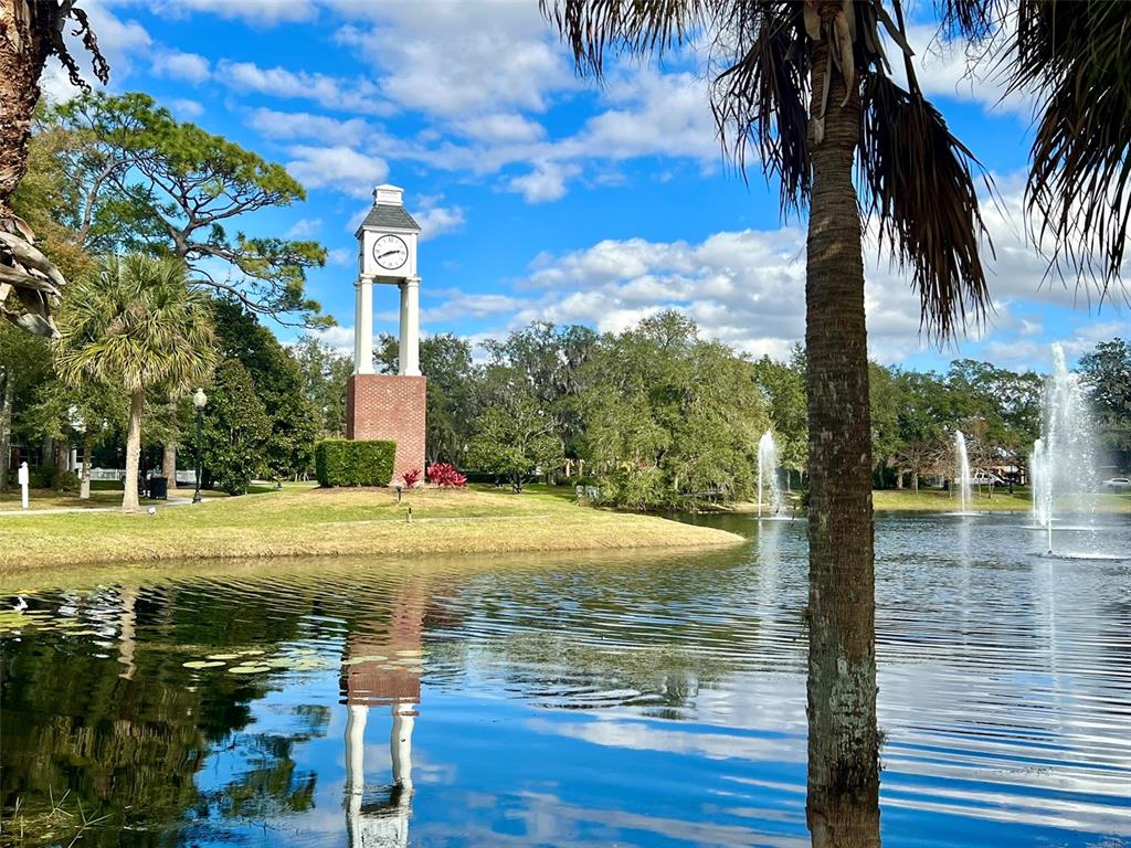 A brick clock tower stands on a grassy bank beside a pond with water fountains — 160 N 4TH STREET, LAKE MARY, FL